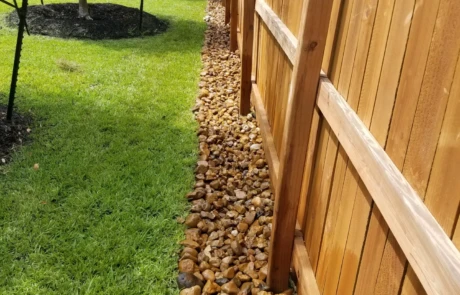 River-rock French drain along a wooden fence line to manage runoff and protect the yard.