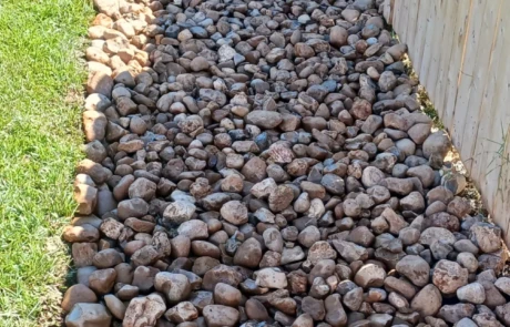 Wide river-rock drainage bed along a fence to move water away from the lawn.