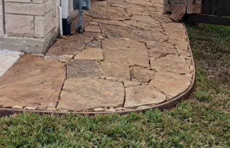 Flagstone side-yard walkway with steel edging along a brick house, leading to a wooden gate.